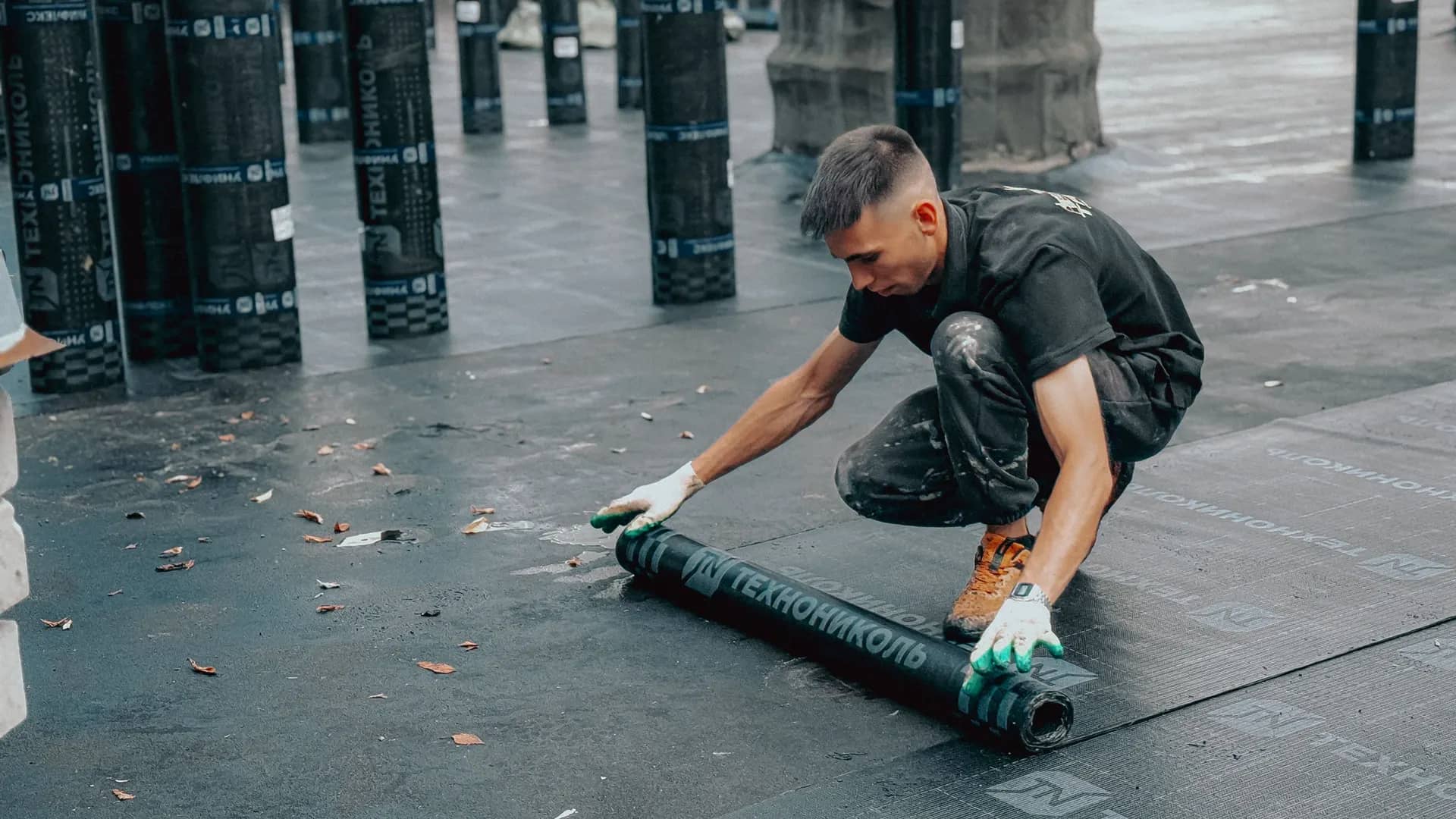 Roofer rolling out a bituminous waterproofing membrane across a flat roof