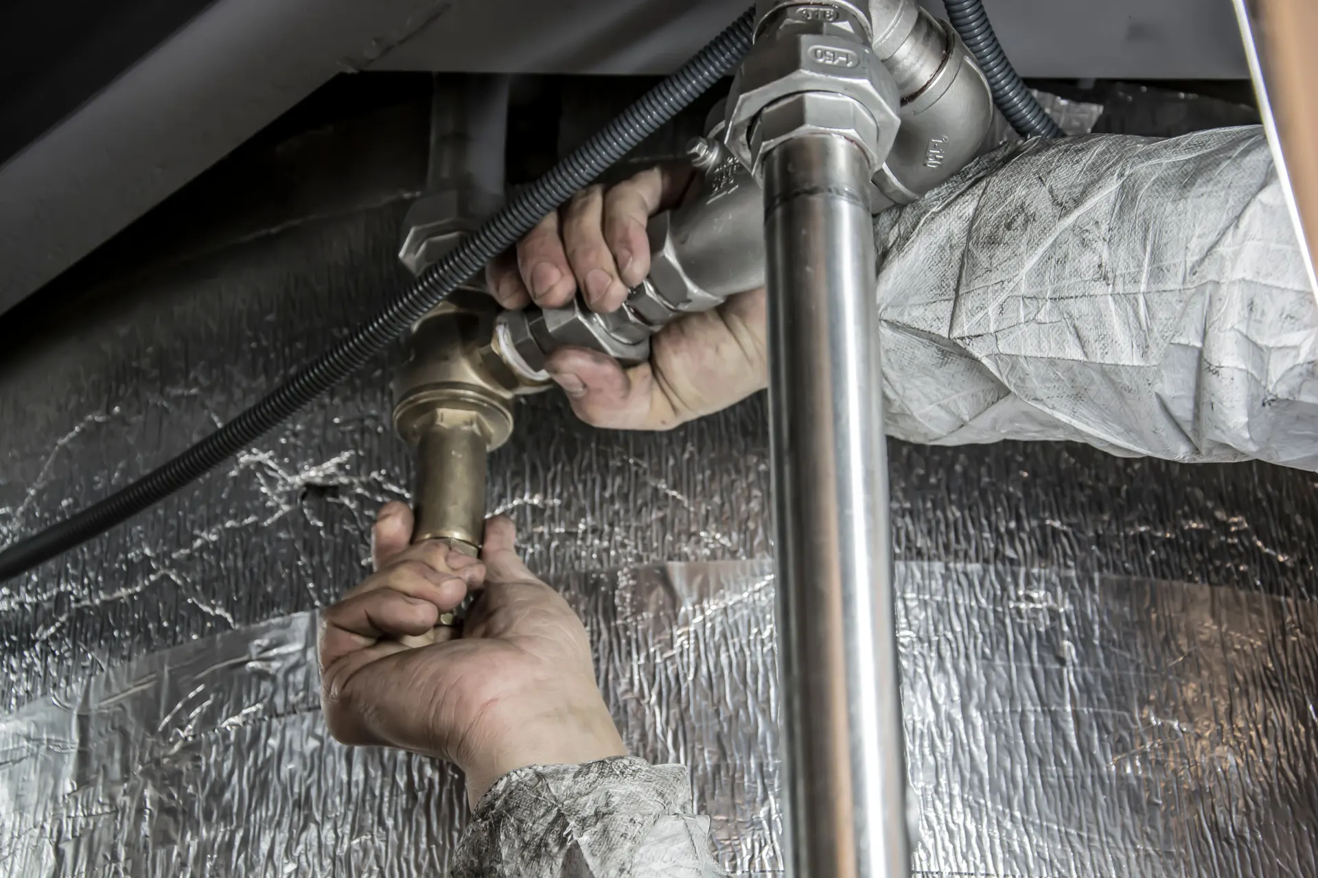 Hands tightening a fitting on an insulated water supply pipe